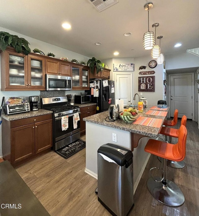 kitchen with hanging light fixtures, a kitchen bar, a kitchen island with sink, appliances with stainless steel finishes, and light wood-type flooring