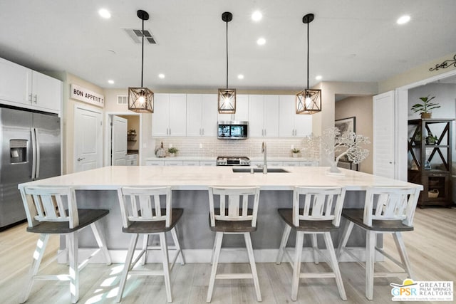 kitchen featuring appliances with stainless steel finishes, decorative light fixtures, white cabinetry, and a large island with sink