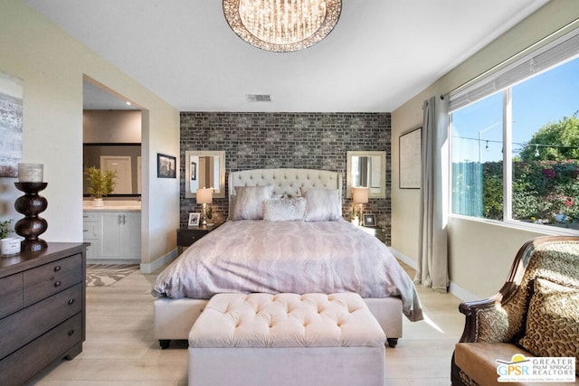 bedroom featuring connected bathroom, a chandelier, and light hardwood / wood-style floors