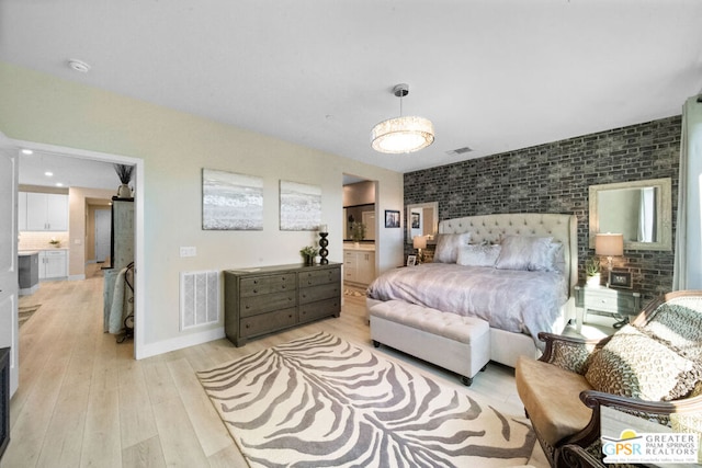 bedroom with ensuite bathroom, light hardwood / wood-style floors, and brick wall