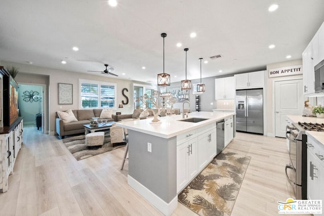 kitchen featuring sink, decorative light fixtures, a kitchen island with sink, white cabinets, and appliances with stainless steel finishes