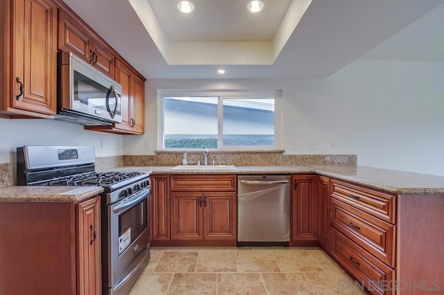 kitchen featuring sink, stainless steel appliances, light stone counters, kitchen peninsula, and a tray ceiling