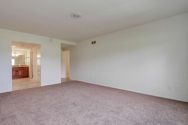 unfurnished bedroom featuring light colored carpet and ensuite bath