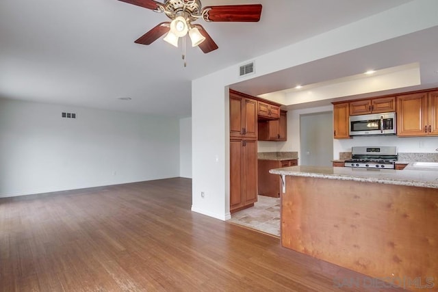 kitchen with sink, ceiling fan, light stone countertops, appliances with stainless steel finishes, and light hardwood / wood-style floors