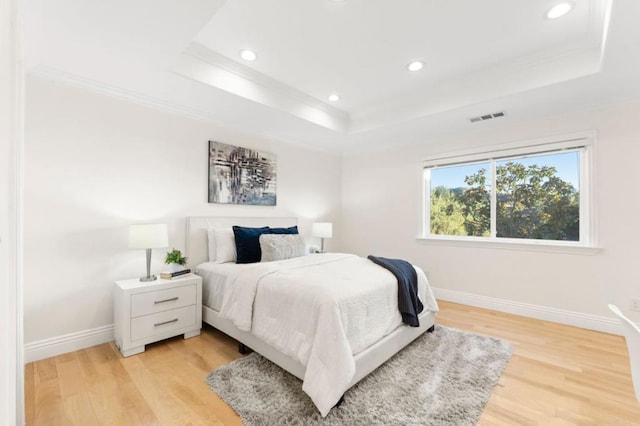 bedroom featuring ornamental molding, a raised ceiling, and light wood-type flooring