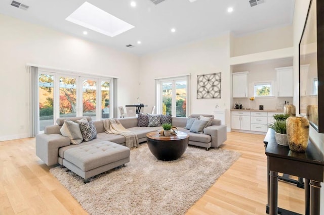 living room featuring a skylight, a towering ceiling, and light hardwood / wood-style floors