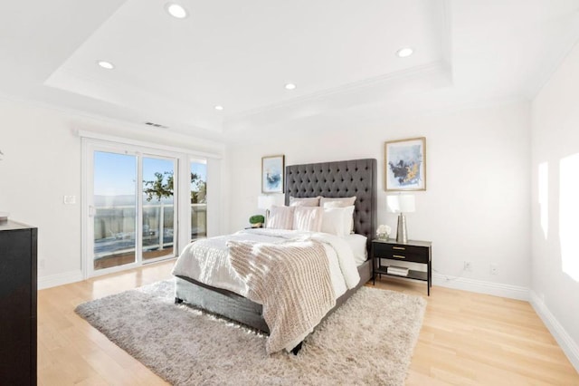 bedroom featuring light wood-type flooring, access to outside, and a tray ceiling