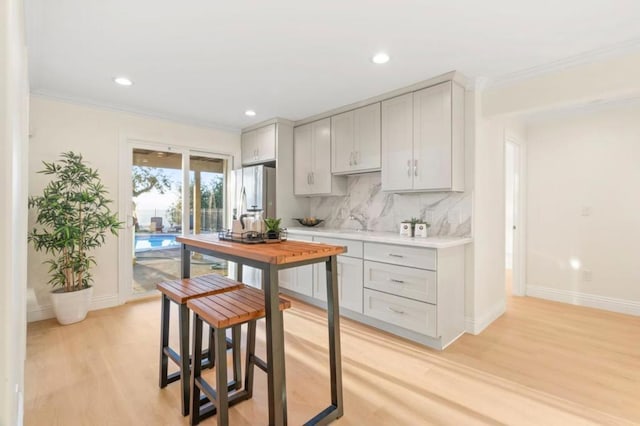 kitchen with light hardwood / wood-style floors, stainless steel fridge, crown molding, and tasteful backsplash