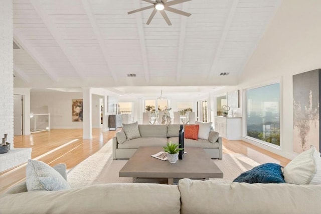 living room with light hardwood / wood-style floors, ceiling fan with notable chandelier, and vaulted ceiling with beams