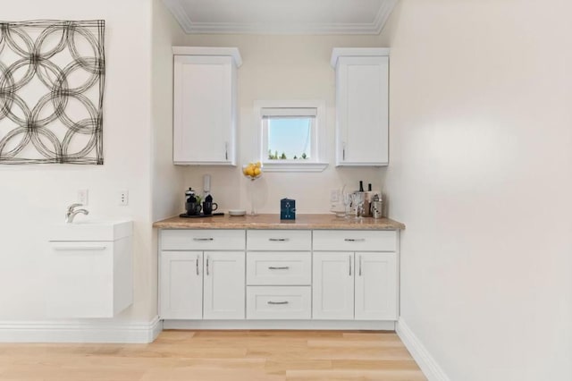 bar with white cabinets, ornamental molding, and light hardwood / wood-style flooring