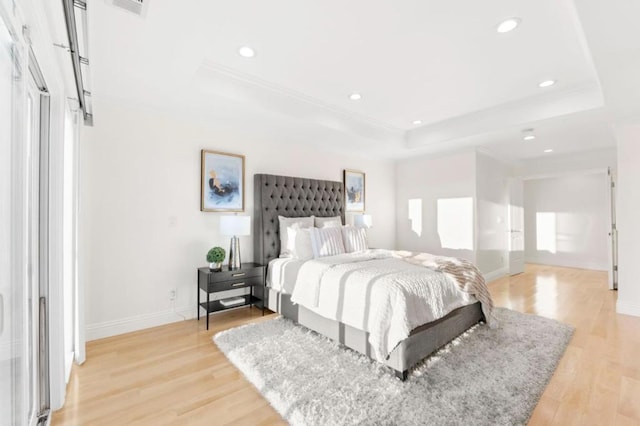 bedroom with ornamental molding, light hardwood / wood-style flooring, and a raised ceiling