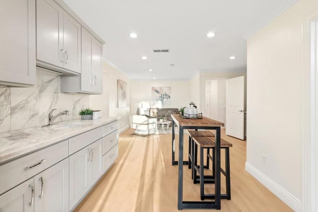 kitchen with light hardwood / wood-style floors, decorative backsplash, crown molding, light stone counters, and sink