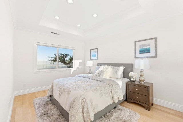 bedroom with light hardwood / wood-style floors, crown molding, and a raised ceiling