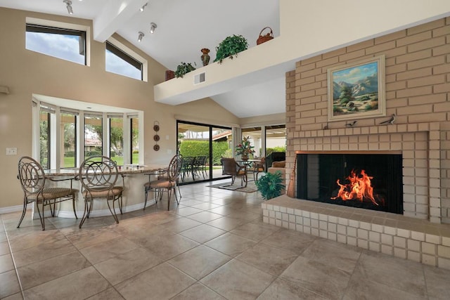 living room with beamed ceiling, light tile patterned flooring, a wealth of natural light, and a brick fireplace