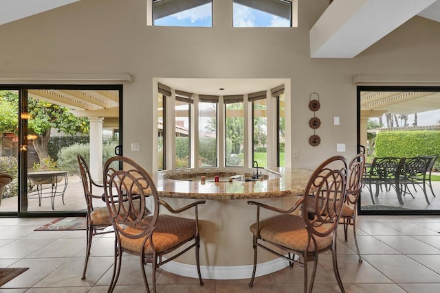 tiled dining space featuring decorative columns and high vaulted ceiling