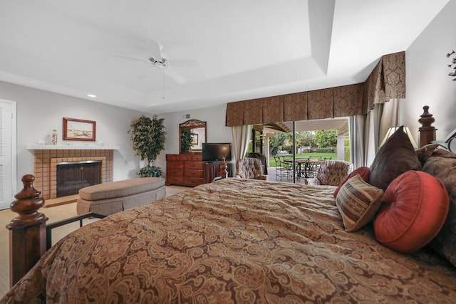 bedroom with access to exterior, a raised ceiling, a brick fireplace, and ceiling fan