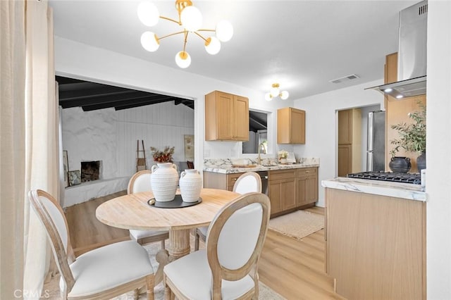 dining space with sink, a premium fireplace, beamed ceiling, a notable chandelier, and light hardwood / wood-style floors