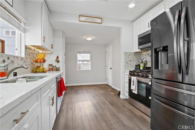 kitchen with white cabinets, sink, light wood-type flooring, appliances with stainless steel finishes, and tasteful backsplash