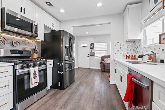 kitchen with white cabinets, sink, light hardwood / wood-style flooring, decorative backsplash, and stainless steel appliances