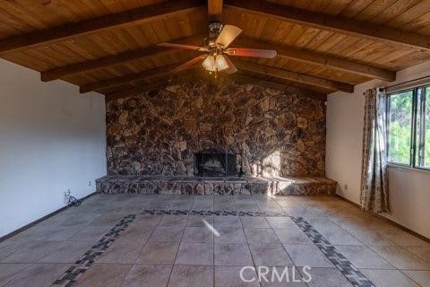 unfurnished living room with ceiling fan, lofted ceiling with beams, a stone fireplace, and wooden ceiling