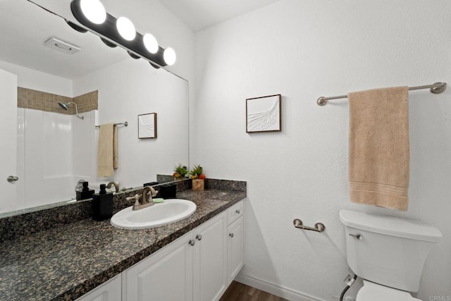 bathroom with tiled shower, hardwood / wood-style floors, vanity, and toilet