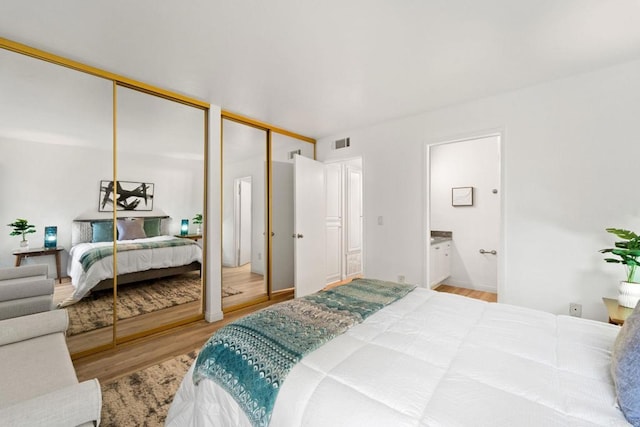 bedroom featuring ensuite bath, multiple closets, and hardwood / wood-style flooring