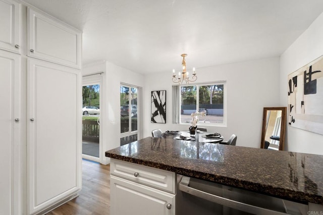 kitchen featuring dark stone counters, white cabinets, stainless steel dishwasher, light hardwood / wood-style floors, and a chandelier