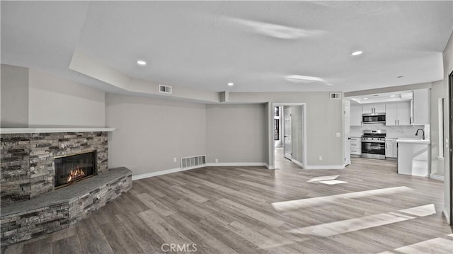 unfurnished living room with light wood-type flooring and a stone fireplace