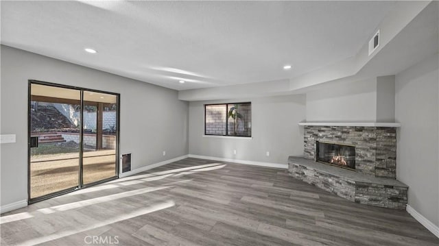 unfurnished living room with a stone fireplace, a healthy amount of sunlight, and wood-type flooring