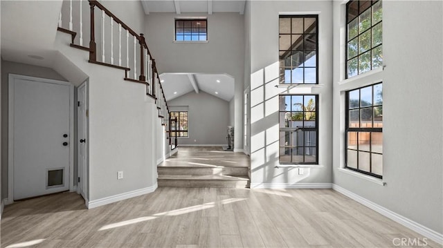 foyer with high vaulted ceiling, a wealth of natural light, and light hardwood / wood-style flooring