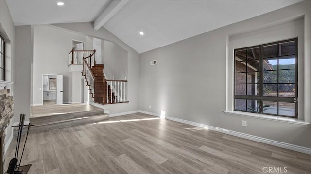 unfurnished living room with vaulted ceiling with beams, light wood-type flooring, and a stone fireplace