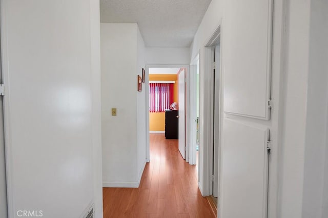 corridor with a textured ceiling and light hardwood / wood-style flooring