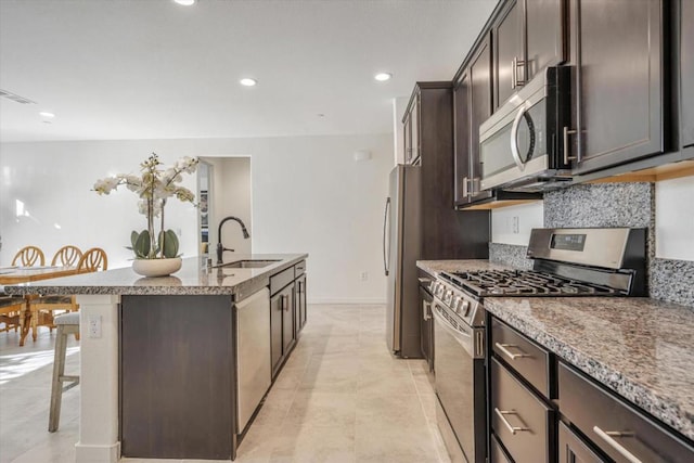 kitchen with sink, appliances with stainless steel finishes, a kitchen island with sink, dark brown cabinets, and a kitchen bar