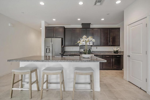 kitchen with stainless steel refrigerator with ice dispenser, dark brown cabinetry, a breakfast bar, and a kitchen island with sink