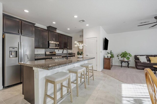 kitchen featuring a breakfast bar, sink, dark brown cabinets, a center island with sink, and stainless steel appliances