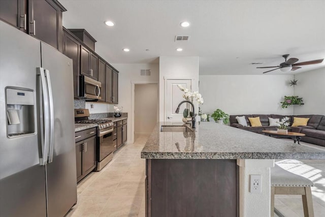 kitchen with dark brown cabinetry, a kitchen bar, sink, stainless steel appliances, and a kitchen island with sink