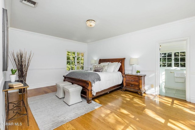 bedroom with wood-type flooring, crown molding, and ensuite bath