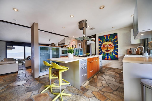 kitchen featuring sink, stainless steel gas cooktop, lofted ceiling, a breakfast bar, and a kitchen island