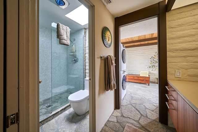 bathroom featuring toilet, walk in shower, and stacked washer and clothes dryer