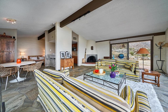 living room featuring lofted ceiling with beams, a large fireplace, and a textured ceiling