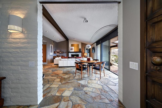 dining area with lofted ceiling with beams, a fireplace, and a textured ceiling