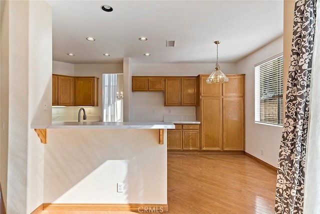 kitchen with kitchen peninsula, a kitchen bar, sink, light hardwood / wood-style flooring, and hanging light fixtures