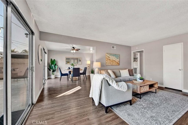 living room with a textured ceiling, ceiling fan, and dark wood-type flooring