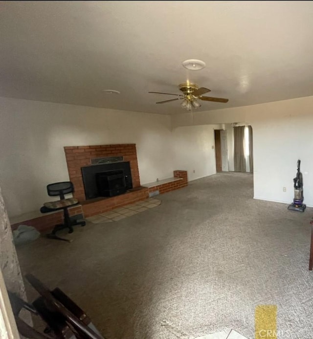 unfurnished living room featuring carpet, ceiling fan, and a brick fireplace