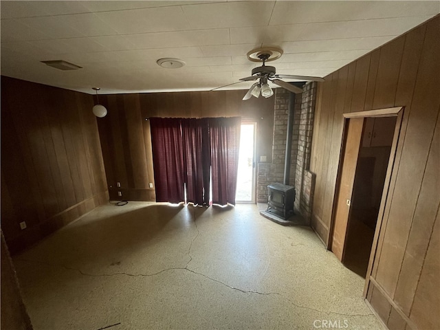 unfurnished room featuring a wood stove, ceiling fan, and wood walls