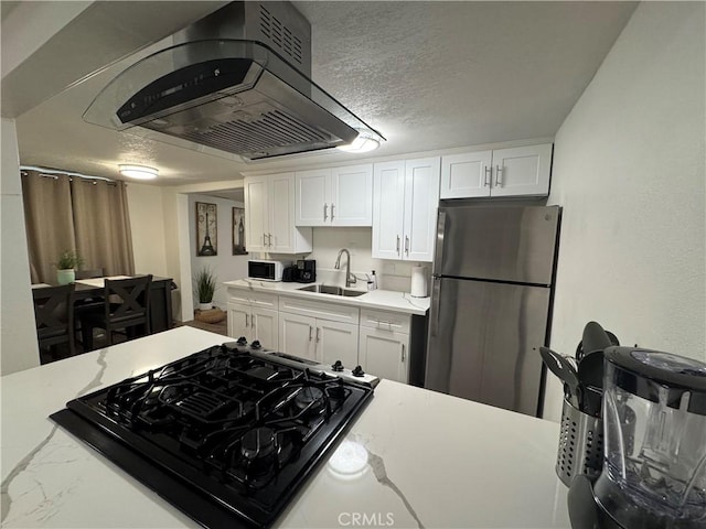 kitchen with a textured ceiling, island range hood, sink, white cabinets, and stainless steel refrigerator