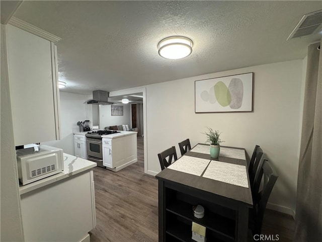 kitchen featuring dark wood-type flooring, gas range, a textured ceiling, white cabinetry, and island exhaust hood