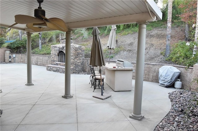 view of patio with exterior kitchen, an outdoor stone fireplace, ceiling fan, a grill, and a bar