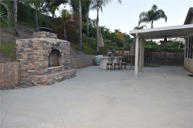 view of patio with ceiling fan, exterior bar, and an outdoor stone fireplace