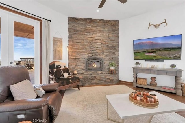 living room with a stone fireplace, ceiling fan, and wood-type flooring